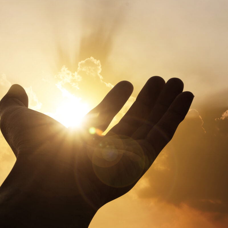 Hand reaching toward sunlight in golden sky
