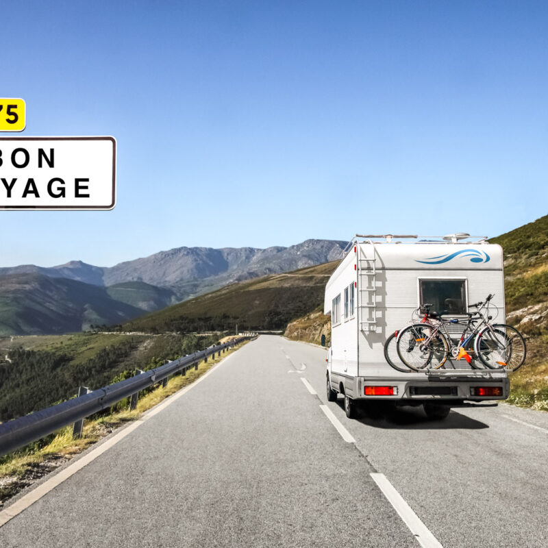 Motorhome with bicycles on mountain road near Bon Voyage sign