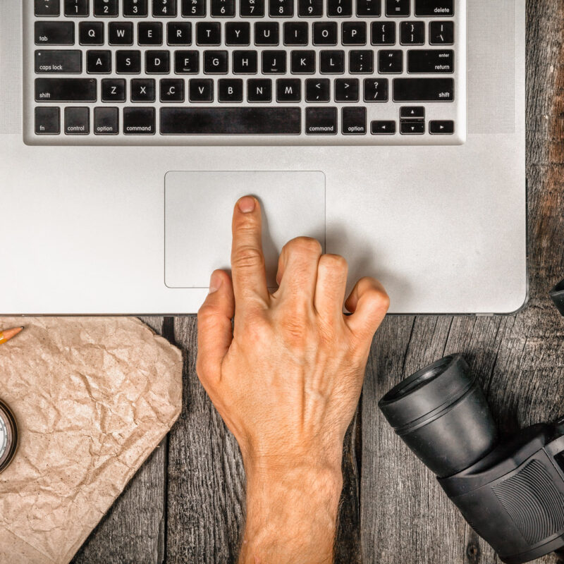 Laptop with hand, binoculars, compass, and map on desk