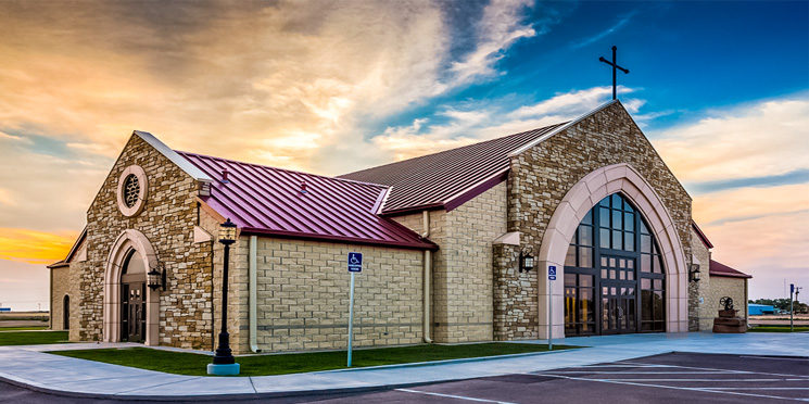 Stone church building with red metal roof at sunset