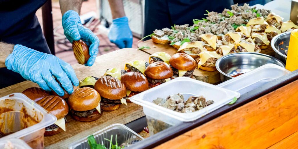 Workers assembling cheeseburgers at a catered food station