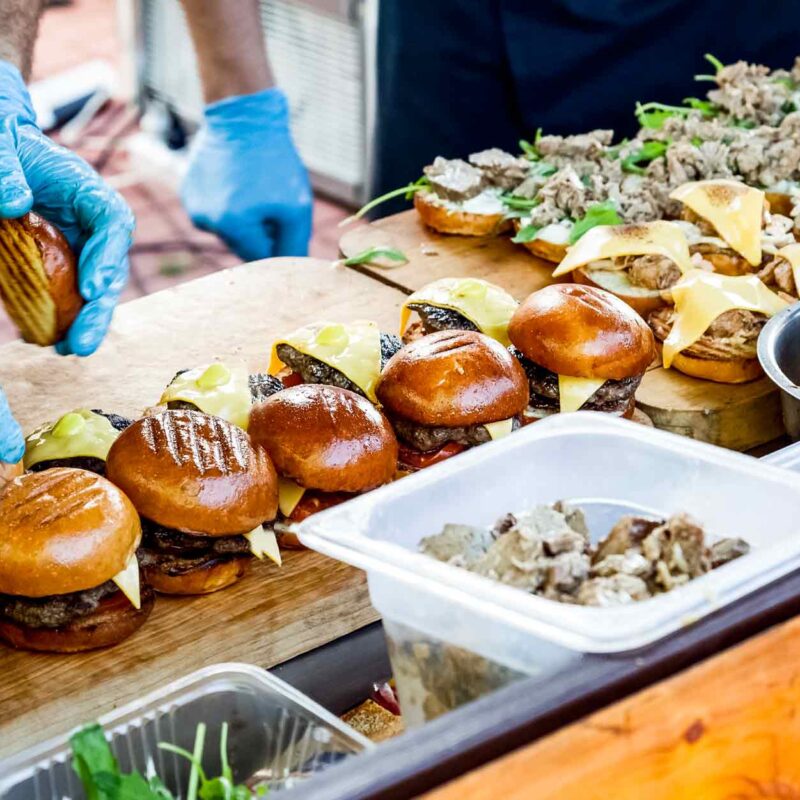 Workers assembling cheeseburgers at a catered food station