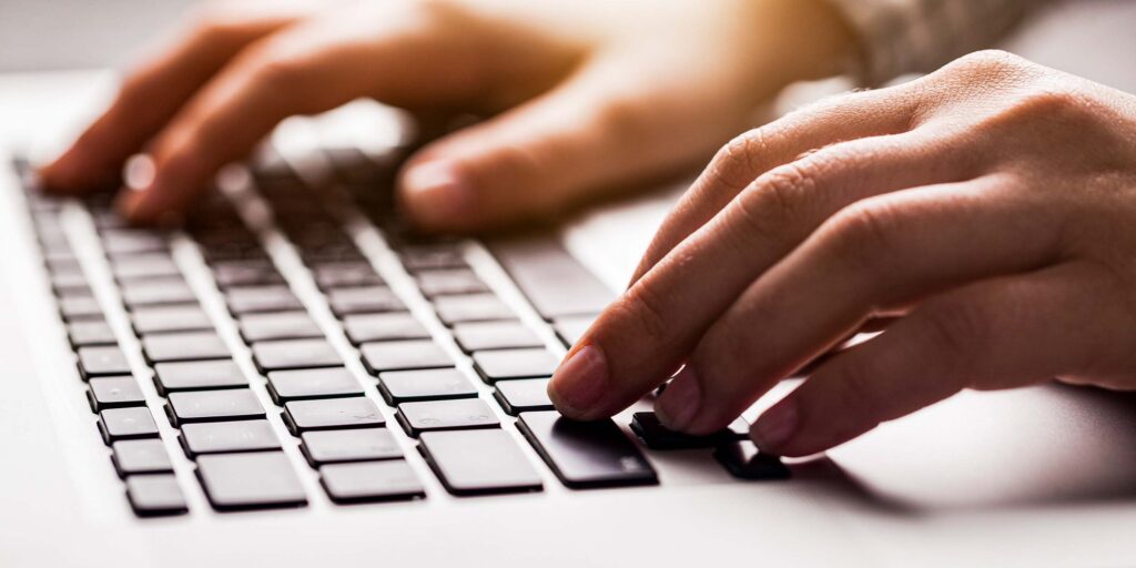 Hands typing on laptop keyboard in close-up computer work scene