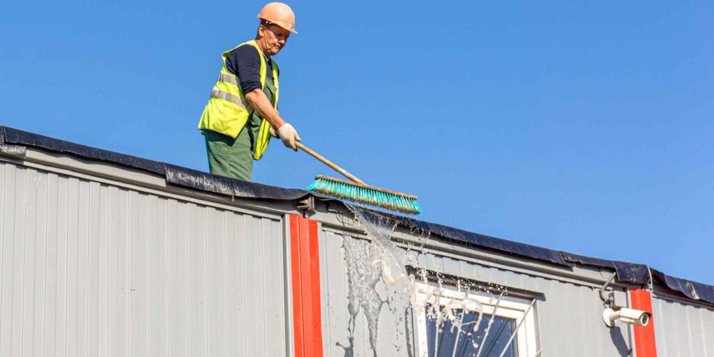 Worker cleaning roof of metal building exterior