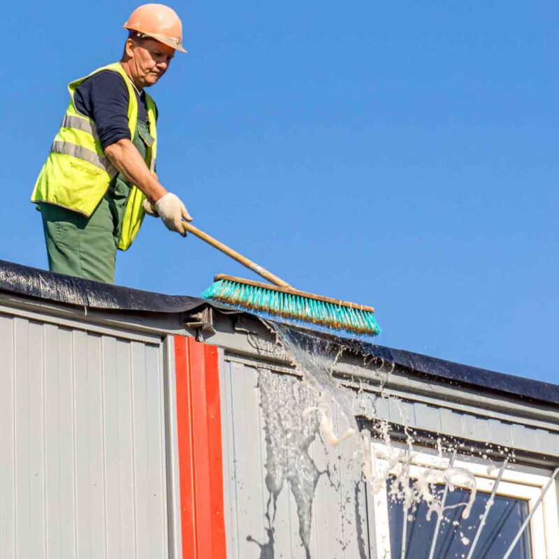 Worker cleaning roof of metal building exterior