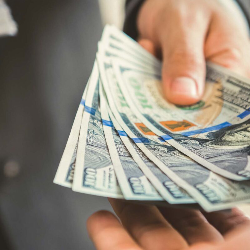 Hand exchanging cash with hundred-dollar bills