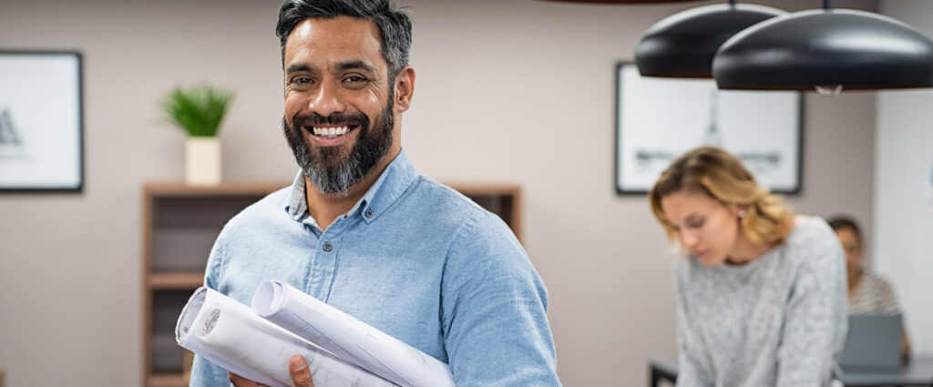 Smiling man holding building plans in office team setting