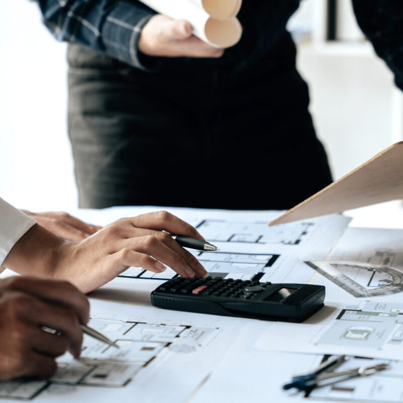 Team reviewing steel building blueprints with calculator and plans
