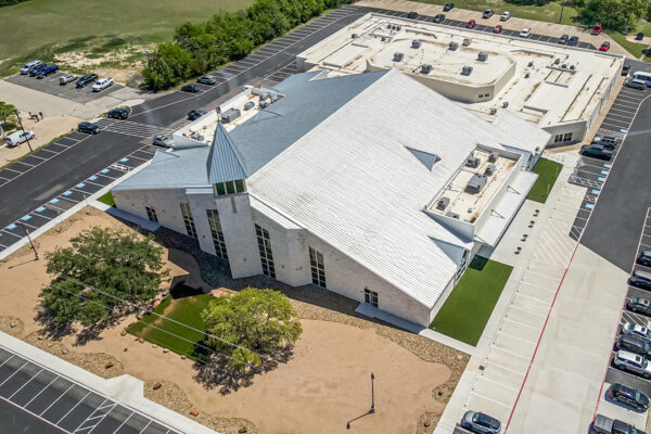 Aerial view of a modern metal church building with a steel roof, surrounded by parking and landscaped areas.