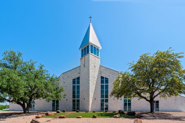 Stone church building with steeple and cross under blue sky