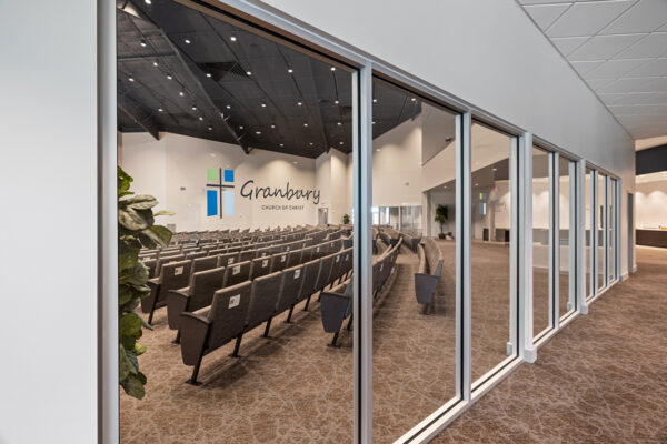 Metal church interior with seating, viewed through glass, featuring a cross and religious symbols; a modern steel building.