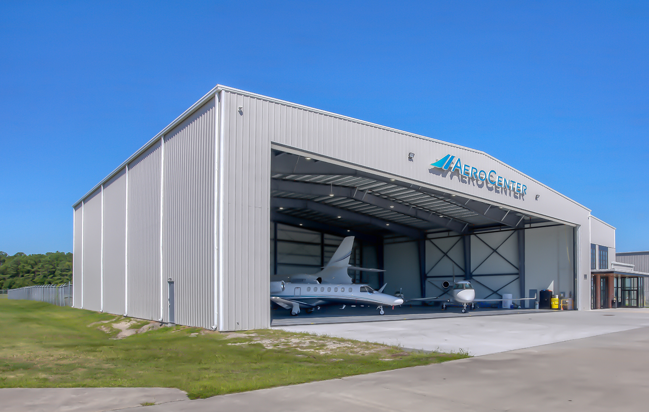 Steel aviation hangar with planes inside, under clear blue sky.