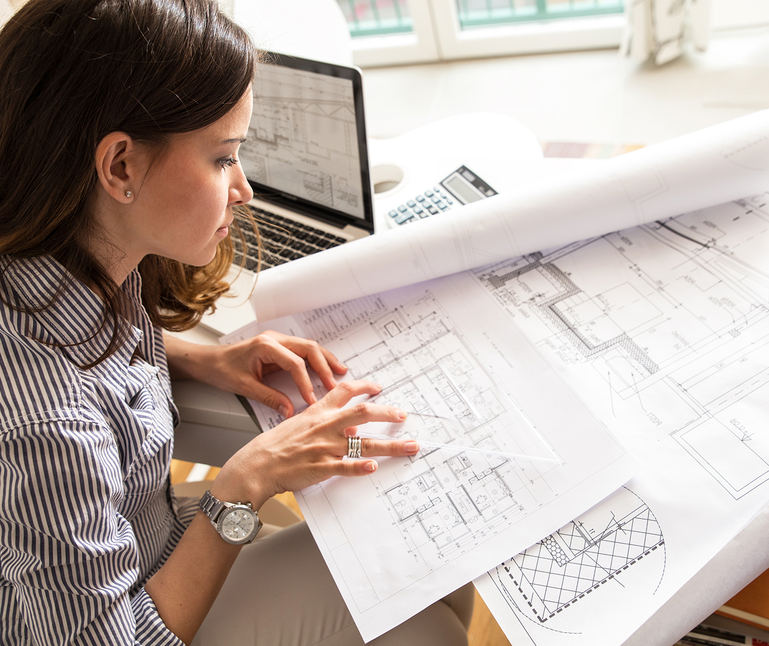 Architect reviewing blueprints for steel building design on laptop.