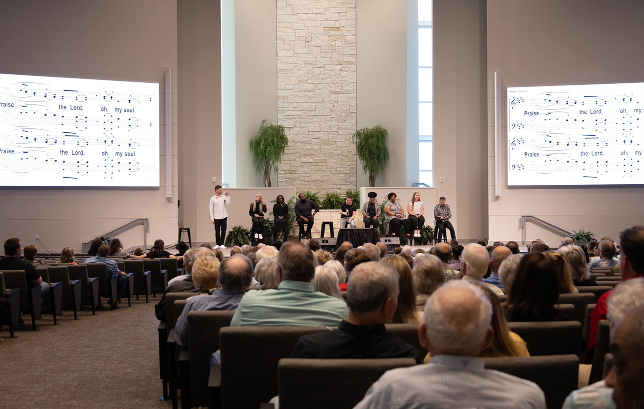 Congregation gathered inside metal church for a service, with worship leaders on stage in religious steel building.