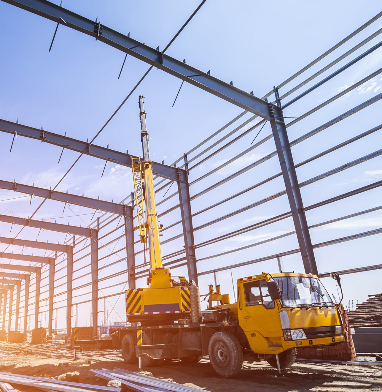 Yellow crane truck in sunny industrial construction site with steel framework.