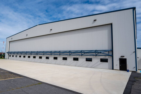 Large white steel aircraft hangar with concrete apron