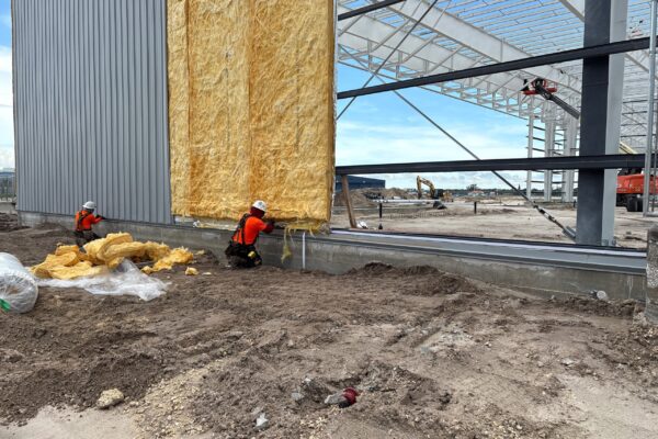Workers installing insulation on steel building construction site