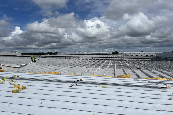 Steel building roof installation with construction worker under clouds