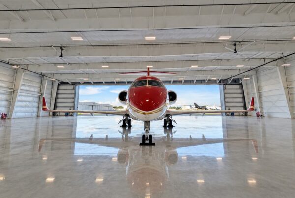 Front view of a red private jet centered inside a pre-engineered steel airplane hangar at Skybridge Miami Opa-Locka Airport, with the open hangar door and flight line behind it