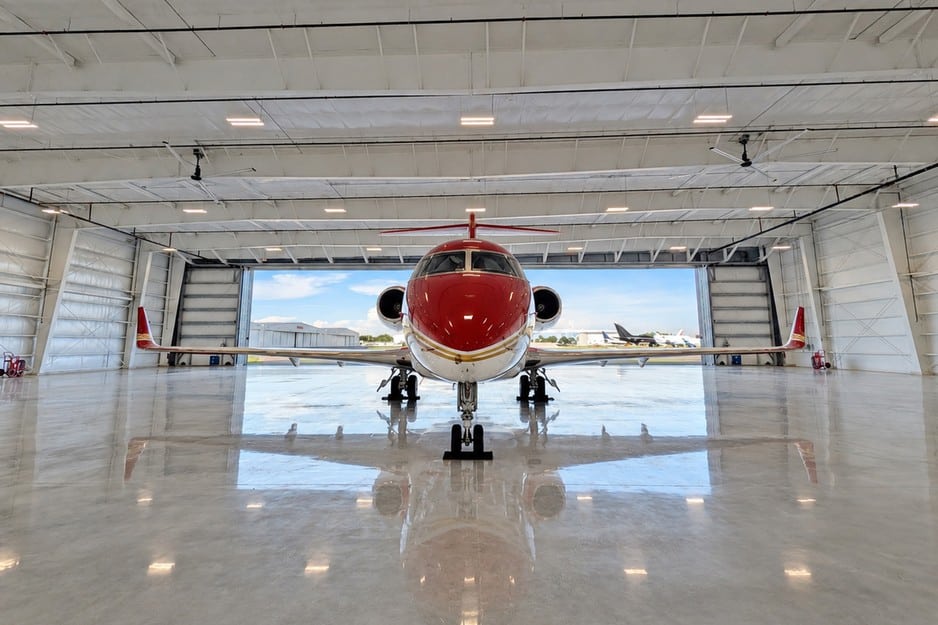 Front view of a red private jet centered inside a pre-engineered steel airplane hangar at Skybridge Miami Opa-Locka Airport, with the open hangar door and flight line behind it