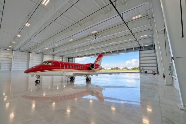 Side view of a red private jet inside a clear span pre-engineered steel airplane hangar at Skybridge Miami Opa-Locka Airport, with the hangar door open behind it