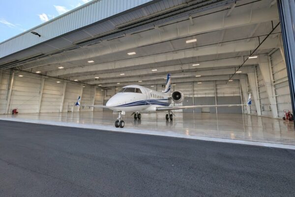 White business jet parked just inside the open door of a pre-engineered steel airplane hangar at Skybridge Miami Opa-Locka Airport
