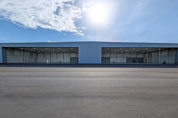 Exterior of a pre-engineered steel airplane hangar building at Skybridge Miami Opa-Locka Airport with two wide hangar doors open to the apron