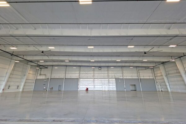 Wide view of an empty pre-engineered steel airplane hangar at Skybridge Miami Opa-Locka Airport showing rigid frames, ceiling fans, and an open floor with no interior columns