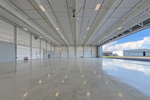 Interior of a pre-engineered steel airplane hangar at Skybridge Miami Opa-Locka Airport showing exposed roof framing, insulated wall panels, and an open hangar door