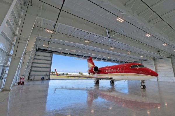 Red private jet parked inside a pre-engineered steel airplane hangar at Skybridge Miami Opa-Locka Airport, hangar door open to the airfield