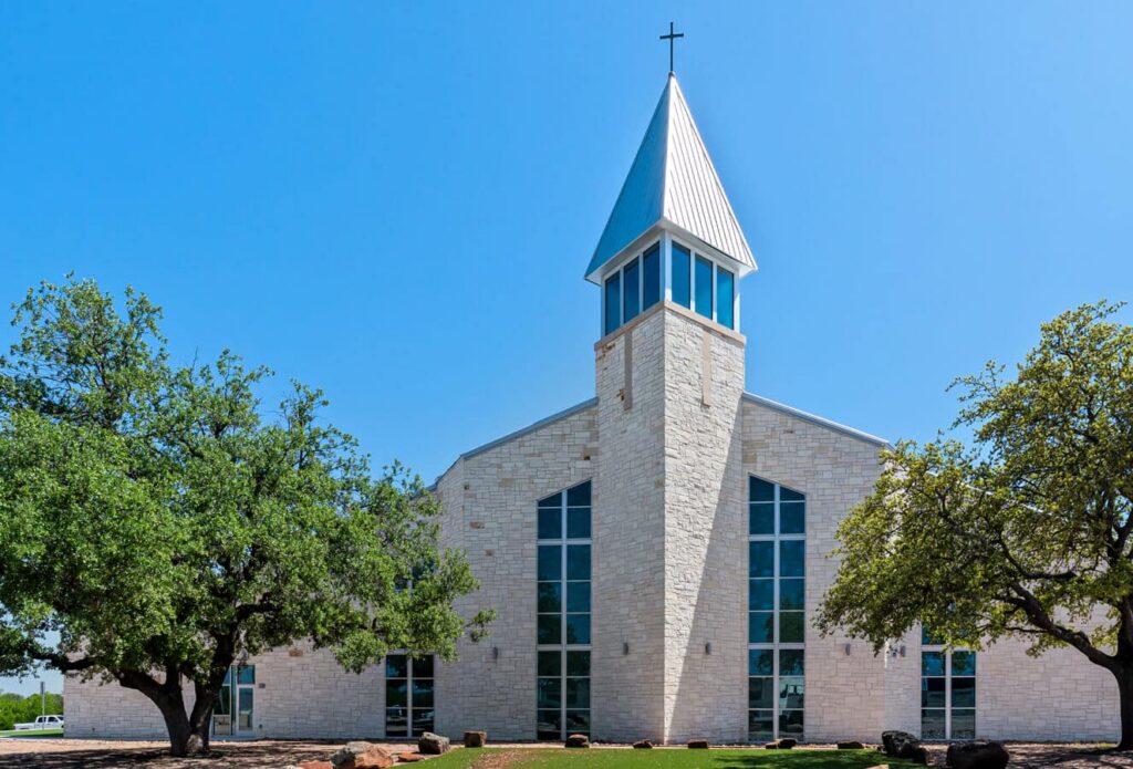 Metal church building in Granbury, TX with a stone facade, open steeple, and tall arched windows