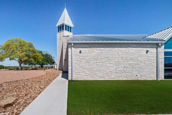 Side view of a metal church building in Granbury, TX with a stone exterior wall, standing seam metal roof, and steeple tower