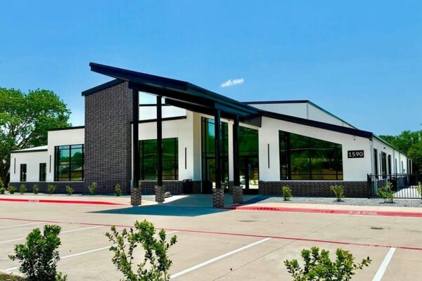 Front elevation of Zion Church, a metal church campus in Richardson, TX, with a brick tower and covered drop-off canopy