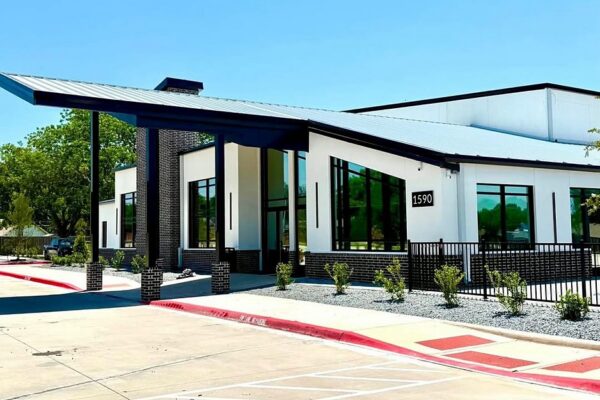 Covered drop-off canopy with a metal roof extending from the entry of a metal church campus in Richardson, TX